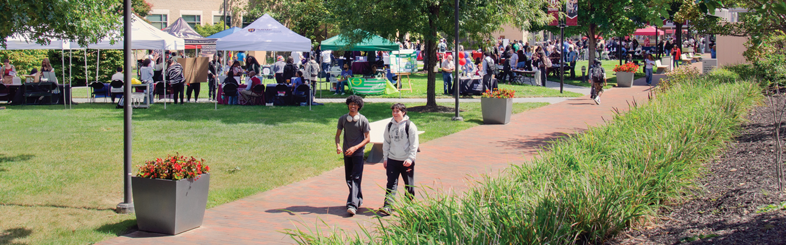 Howard Community College campus during a sunny student activities fair with tents on the quad and students walking along a brick pathway