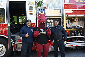 Two emergency personnel stand on either side of a red dragon mascot wearing a