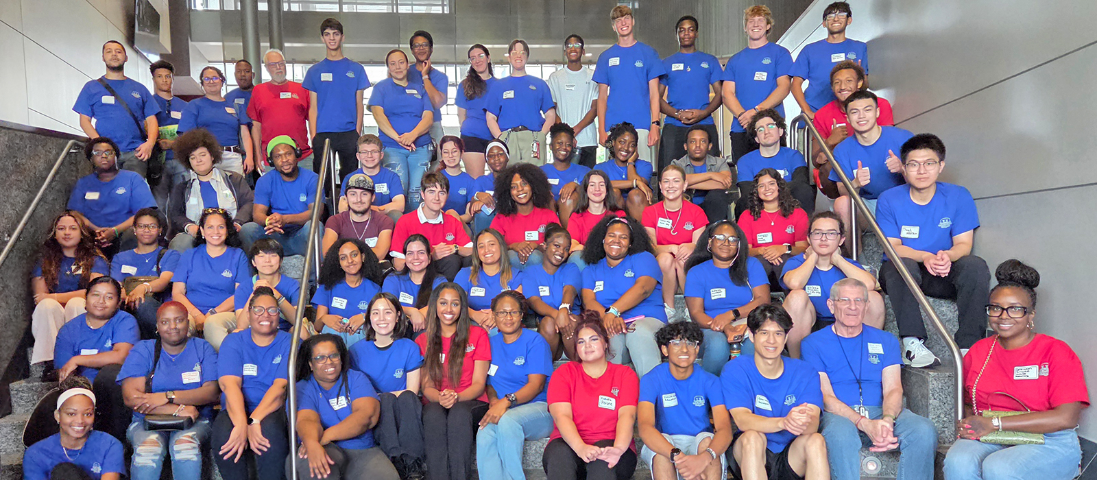 Large group of Howard Community College Honors students and faculty pose together on a staircase, with most wearing blue or red HCC shirts.