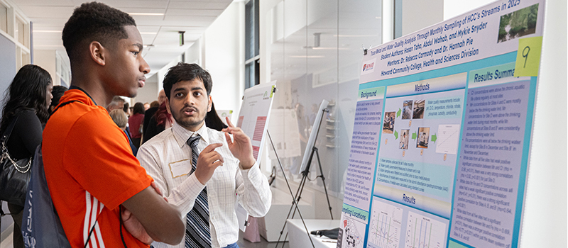 Two HCC students discuss a research project presented on a poster board during a campus research event.